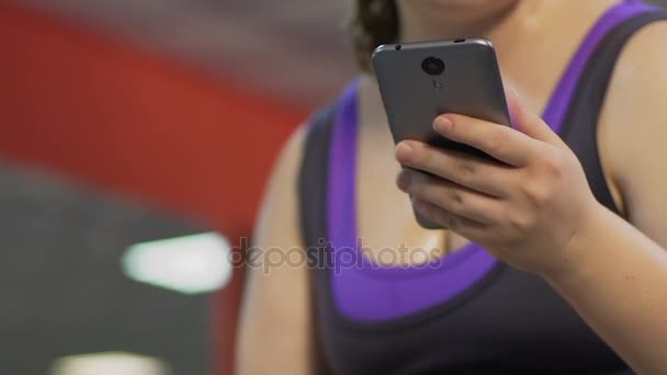 Chica con peso extra levantamiento de pesas, desplazamiento de la pantalla del teléfono celular, distracción — Vídeos de Stock