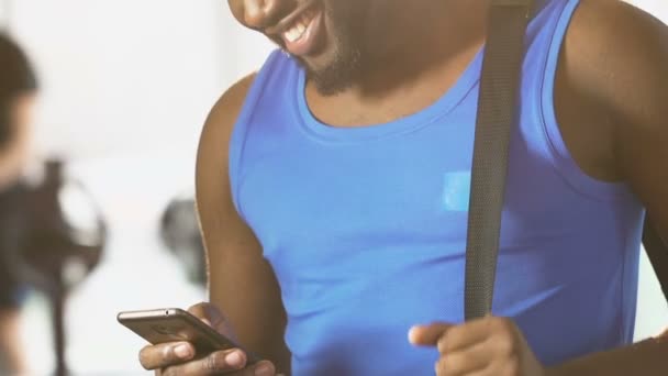 Joven hombre de pie en el gimnasio con bolsa en el hombro, mensaje de lectura en el teléfono celular — Vídeos de Stock