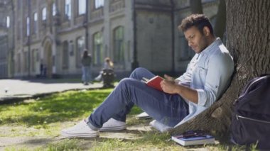 Ağacın altında oturan erkek üniversite öğrenci bilgileri ezberleme kitap okuma