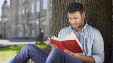 Erkek okuma favori roman kitap göğüs karşı basarak ağacın altında hayal