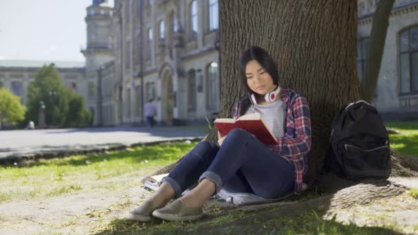 Smíšené žena čtení knihy pod stromeček, tlačí hruď, oblíbená kniha — Stock video
