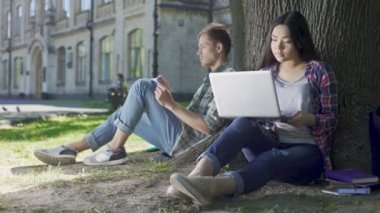 Laptop ve defter, ağacın altında oturup not alma adam kullanan genç kadın