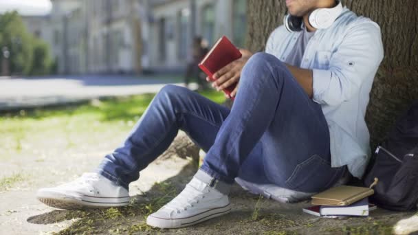 College-Student sitzt unter einem Baum, nimmt Buch zum Lesen, Literaturwissenschaft, Klasse — Stockvideo
