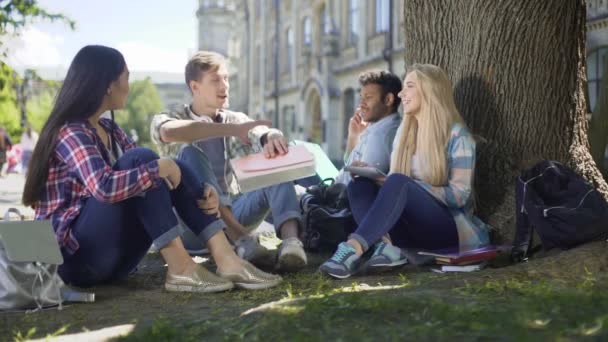 Mladí lidé sedí pod stromem a sdílení myšlenek, členové university kruhu — Stock video