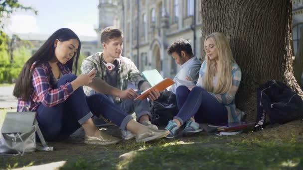 Přátele, jak sedí pod stromem, pomocí telefonů, mluví, komunikace — Stock video