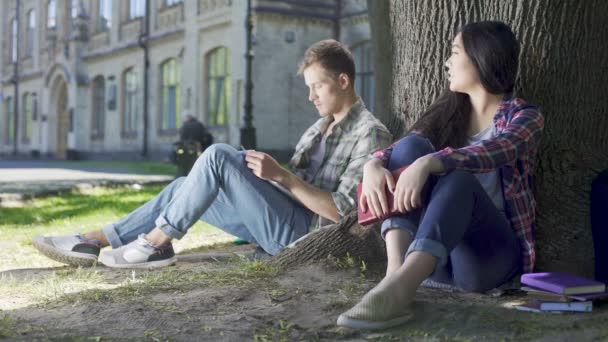 Muž a žena, sedící pod stromem, dívka říká něco, chlap na ni — Stock video
