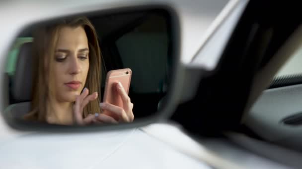 Отражение в зеркале заднего вида, красивая женщина прокручивает новости на мобильном телефоне — стоковое видео