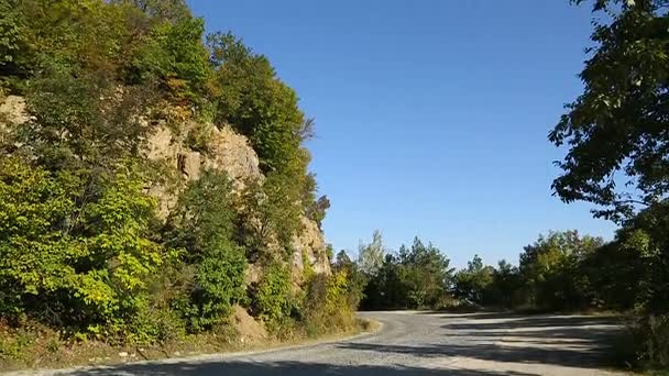 Дорога в горах, высокая скала с деревьями на ней стоит на плече, природа — стоковое видео