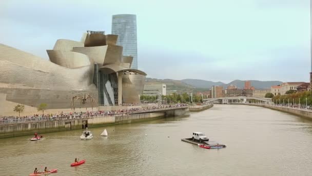 Statua del ragno, folla davanti al moderno edificio dorato di fronte al fiume con barche — Video Stock