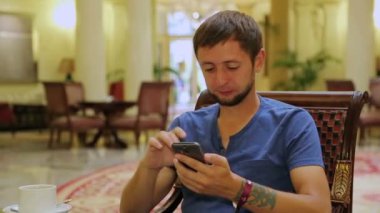 Erkek turistik otel lobisinde bir kahve ile oturan cep telefonu haber okuma