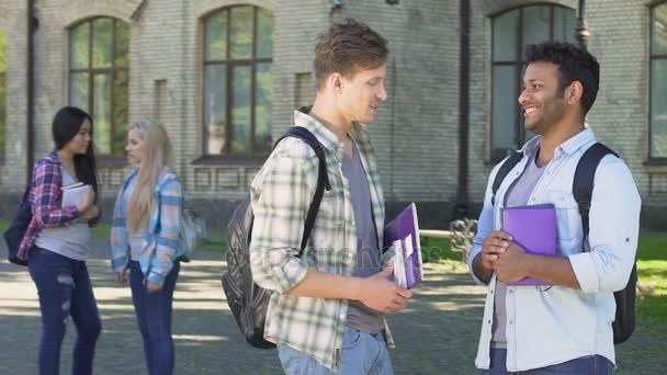 Dos estudiantes masculinos sonrientes hablando de fiesta de graduación cerca de la universidad — Vídeos de Stock