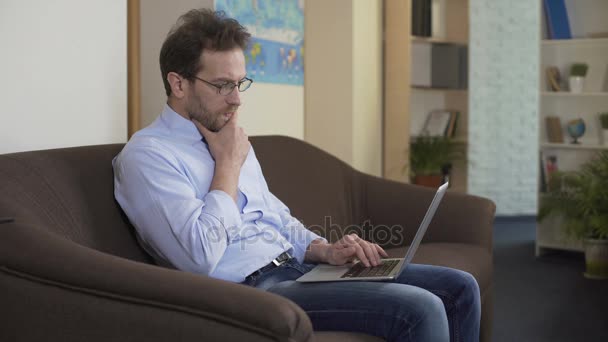 Homem adulto sentado no sofá e navegando redes sociais no laptop, tecnologias — Vídeo de Stock