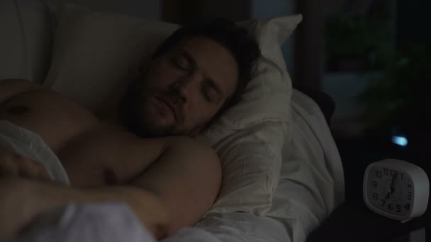 眠い疲れた男の目覚まし時計をオフにします。睡眠不足。ベッドで横になっている男 — ストック動画