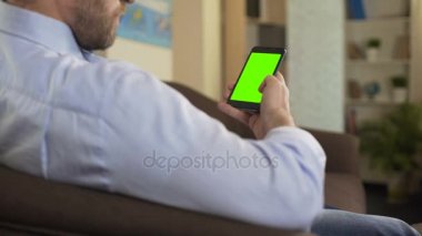 Kanepe üzerinde erkek oturan ve yeşil ekranlı cep telefonu üzerinde kaydırma sakallı app