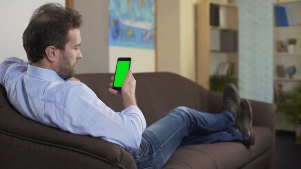 Entspannter Mensch sitzt auf Sofa und sucht Hotel für Urlaub auf dem Smartphone — Stockvideo