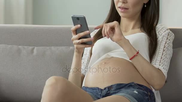 Futura madre desplazándose por la pantalla del teléfono celular, leyendo el blog embarazo, consejos en línea — Vídeo de stock