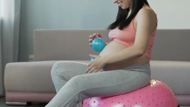 Lady gravid med barn sitter på fitness boll, rullande massage bollar över mage — Stockvideo