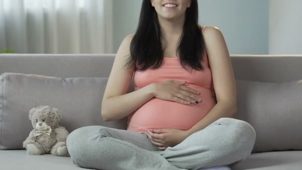 Mulher grávida sentada no sofá, esfregando o estômago e sorrindo, gravidez feliz — Vídeo de Stock