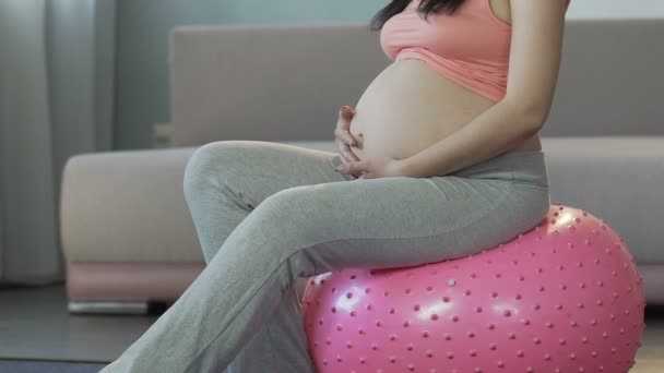 A várandós nő ül a fitness labda, kézenfogva, a gyomor, relaxáció — Stock videók