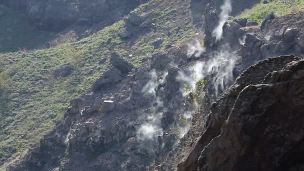 Vapor blanco que sube de debajo de piedras en laderas rocosas día soleado, volcán — Vídeo de stock