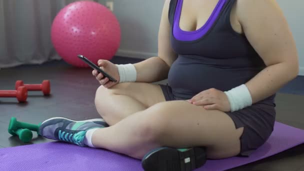 胖胖的女孩滚动无动机而不是锻炼她手机上的应用程序 — 图库视频影像