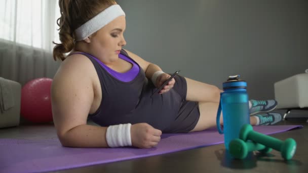 Menina obesa preguiçosa rolando seu telefone em vez de treino esportivo para perda de peso — Vídeo de Stock