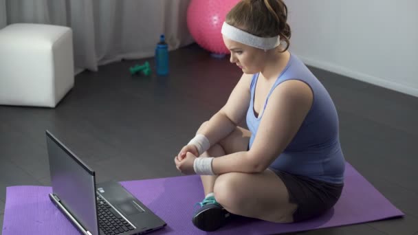 Chica gorda viendo videos en línea con famosos métodos de entrenamiento en su computadora portátil — Vídeos de Stock