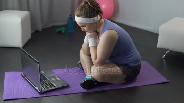 Chubby chica nerviosamente leyendo entrenamiento y plan de dieta de su entrenador en el ordenador portátil — Vídeos de Stock