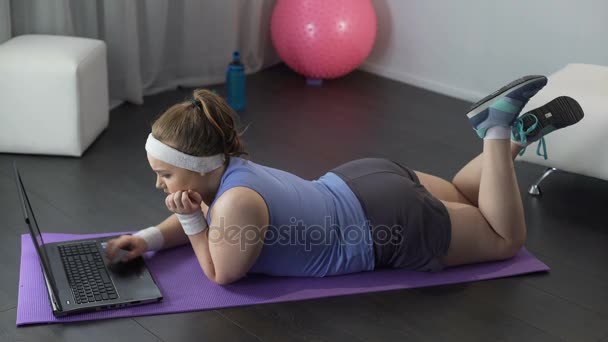 Толстая девушка смотрит уроки фитнеса на своем ноутбуке, готовится к спортивной тренировке — стоковое видео