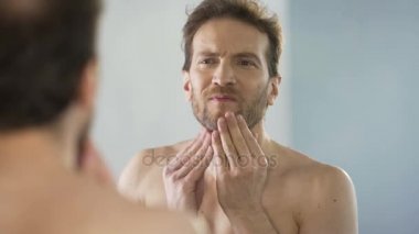 Orta yaşlı adam sakalını ayna, sabah ritüeli eleştirel bakıyor