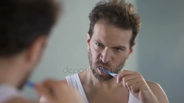 Сонный мужчина чистит зубы, устал от рутины, ходит на работу утром, похмелье — стоковое видео