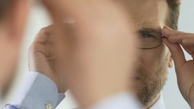 Erkek gözlük takıyor ve aynanın önünde, kötü görme sorunu çatık