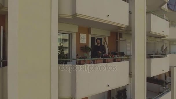 Мужчина пьет кофе, стоит на балконе жилого комплекса, прекрасное утро — стоковое видео