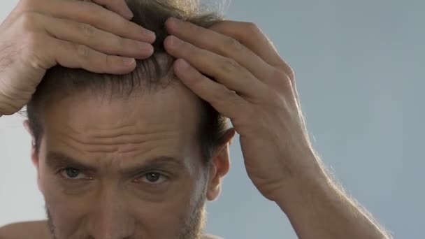 Bearded man standing in front of mirror and looking at his thinning hair, bald — Stock Video