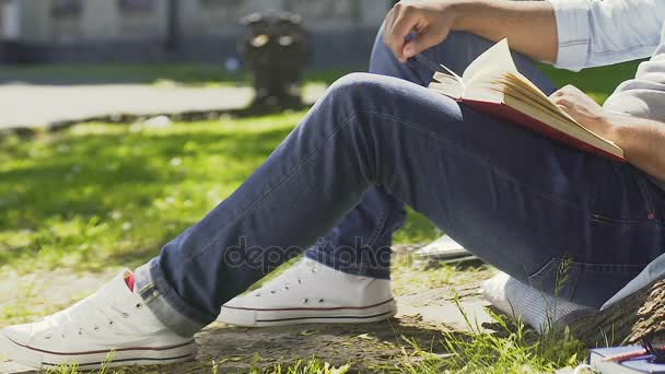 Teenager enthusiastically reading book sitting outdoors and breathing fresh air — Stock Video