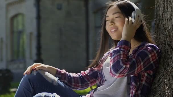 Hermosa estudiante feliz disfrutando de música favorita que suena en sus auriculares — Vídeos de Stock