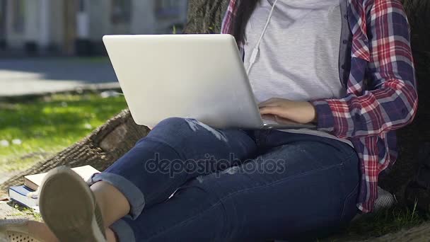 Studentin sitzt mit Laptop im Garten der Universität und chattet online — Stockvideo