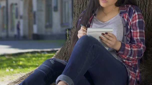 Chica romántica escribiendo poesía de amor, sentado en la sombra de un enorme árbol en el parque de verano — Vídeo de stock