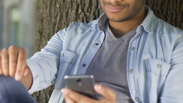 Hombre biracial guapo sonriendo y charlando en las redes sociales, utilizando el teléfono inteligente — Vídeo de stock