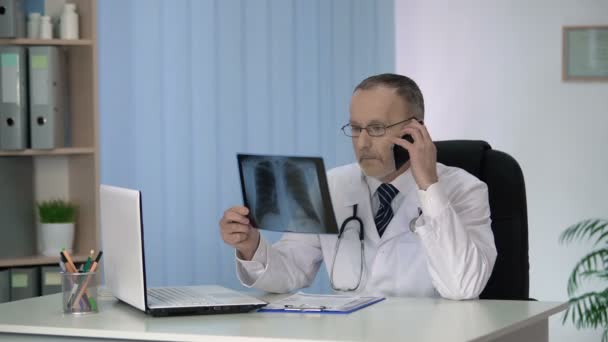 Allgemeinmediziner telefoniert mit seinem Onkologen-Kollegen zum Röntgen der Lunge — Stockvideo