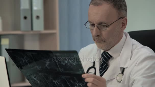 Neurólogo examinando el venograma del paciente y escribiendo sus hallazgos en la tarjeta del paciente — Vídeos de Stock