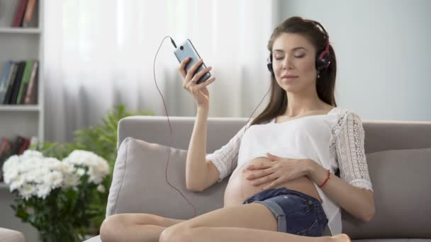 Verwacht dame luisteren naar ontspannende muziek op mobiel en buik wrijven — Stockvideo