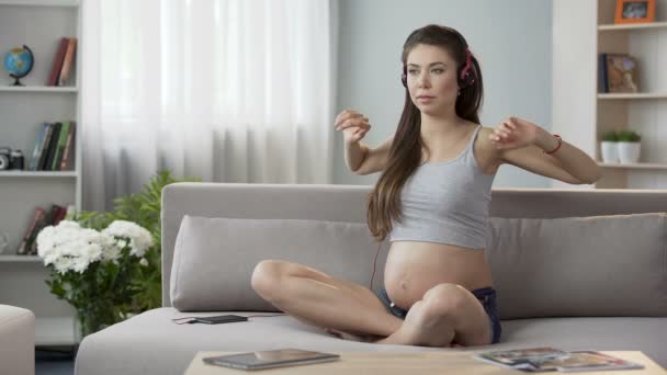 Femme enceinte assis dans des écouteurs exercice, audioguide pour le yoga grossesse — Video