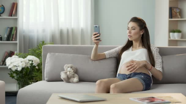 Schwangere mit Kind sitzt auf Sofa und benutzt Handy, Online-Blog — Stockvideo