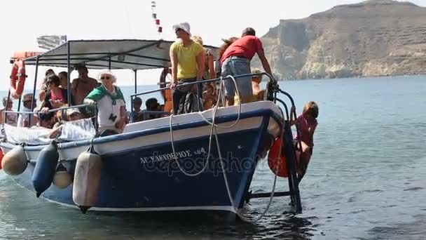 SANTORINI, GREECE - CIRCA JULY 2014: Осмотр достопримечательностей острова. Довольные морскими экскурсиями туристы спускаются с лодки на берег красного пляжа — стоковое видео