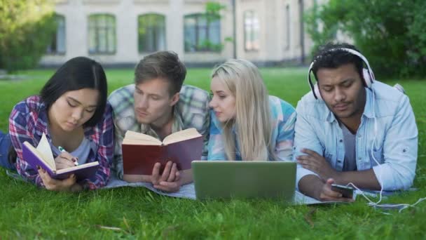 Grupo de amigos tumbados en el césped en el campus y preparándose para la prueba, la vida del estudiante — Vídeos de Stock