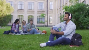 Çimenlerin üzerinde oturan ve kulaklık müzik keyfi yakışıklı İspanyol öğrenci
