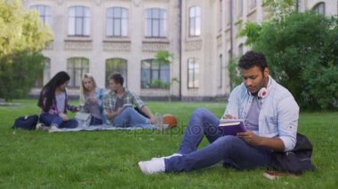 Ödev çimenlerin üzerinde oturan ve kompozisyon, ciddi biracial erkek öğrenci