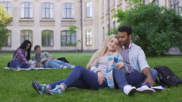 Couple multiracial relaxant sur l'herbe, parlant et souriant, premier amour, étudiants — Video