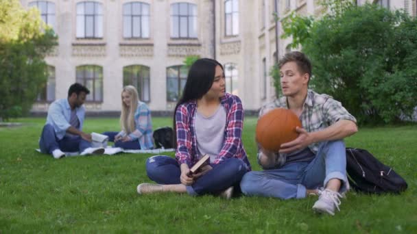 Students sitting on lawn on campus and flirting, male trying to impress girl — Stock Video